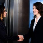 Smiling business people shaking hands at office lobby in front o